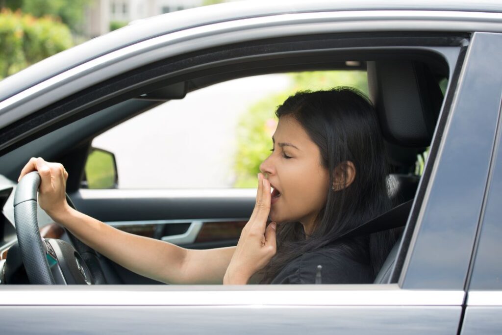 A woman yawning behind the steering wheel of a car.