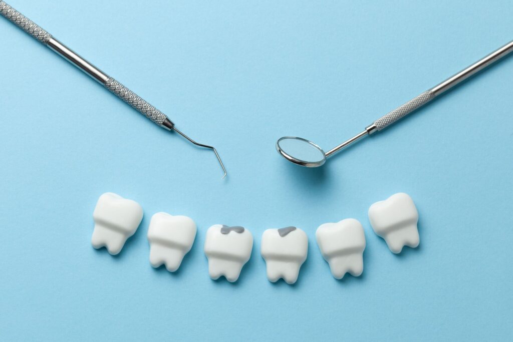 Row of fake teeth with faux gray fillings next to dental instruments on blue background